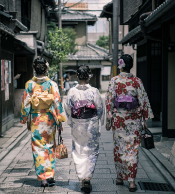 three Asian women, with their backs turned, walking down a street